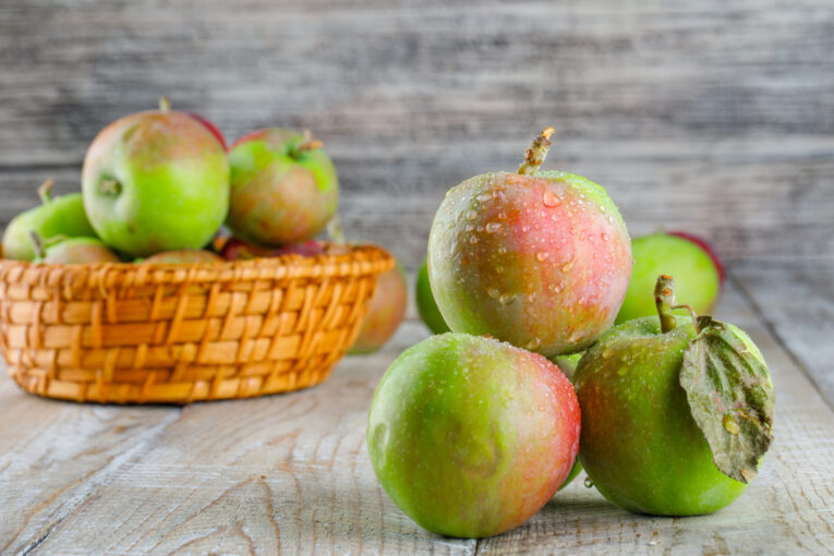 Chilly apples in a wicker basket on a wooden background. side view.